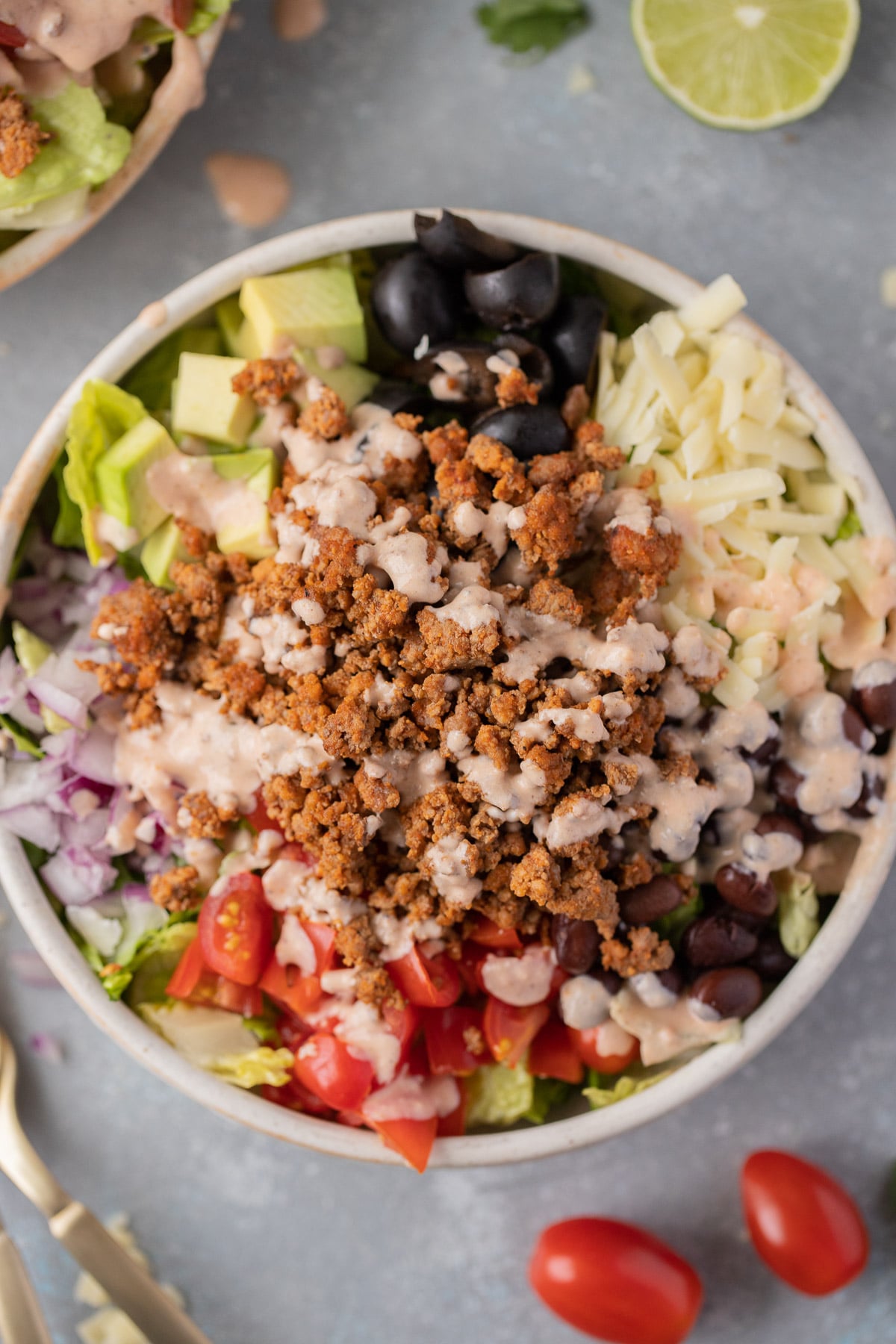 Overhead close up of beef taco salad in a white bowl on a grey background