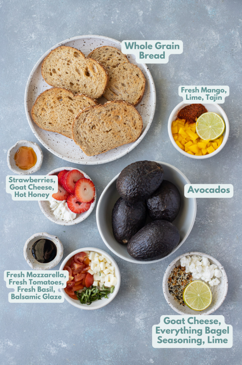 Ingredients for avocado Toast in white bowls: whole grain bread, avocado, goat cheese, everything bagel seasoning, lime, fresh mozzarella, fresh tomatoes, balsamic glaze, fresh basil, strawberries, goat cheese, hot honey, fresh mango, tajin