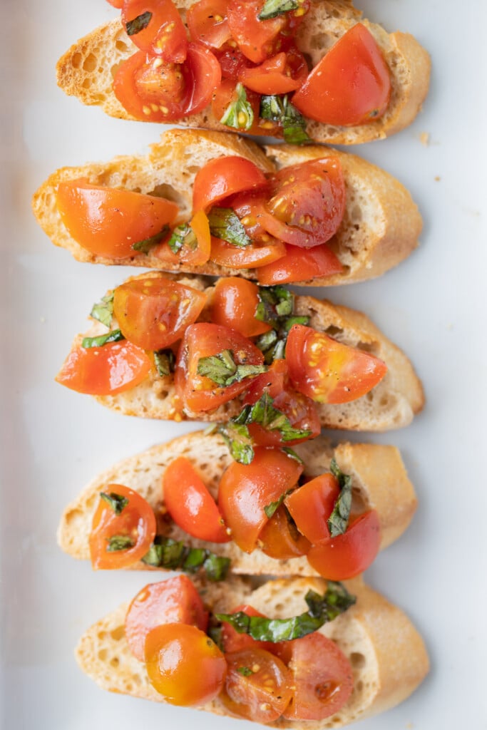 6 Bruschetta baguette toasts in a row on a white platter on a grey background