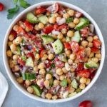 An overhead shot of a white bowl of Mediterranean chickpea salad on a grey background