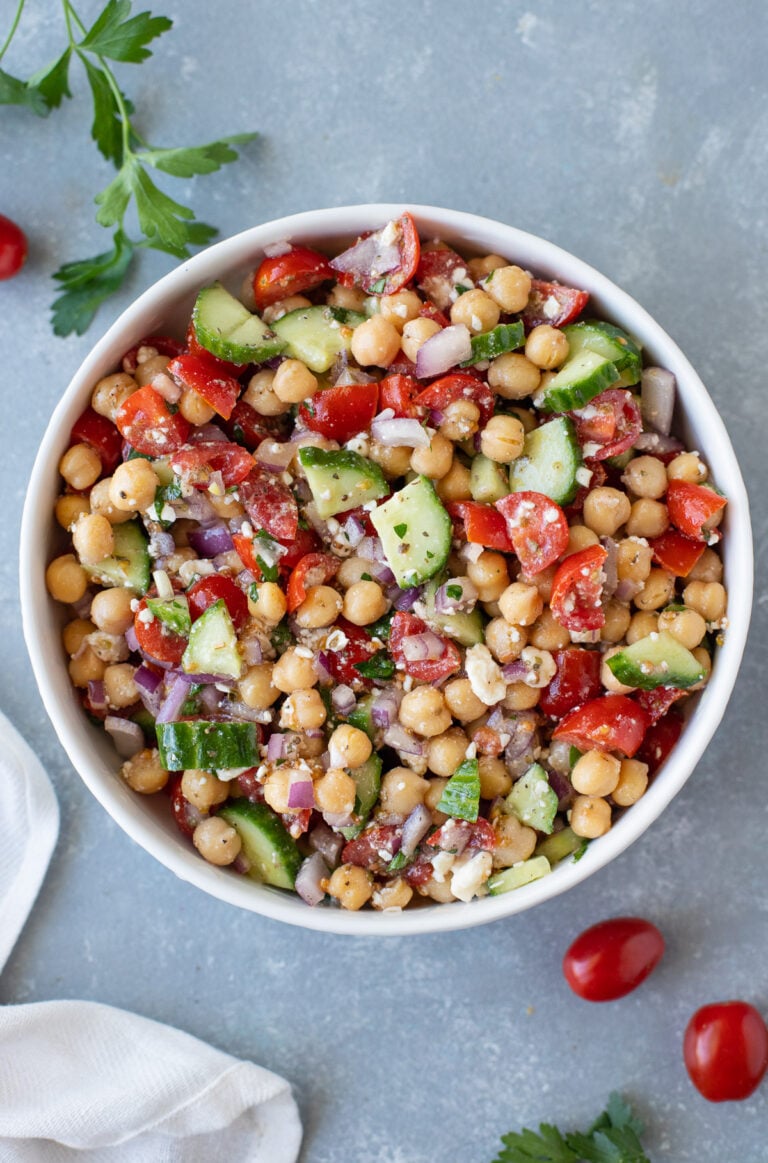 An overhead shot of a white bowl of Mediterranean chickpea salad on a grey background