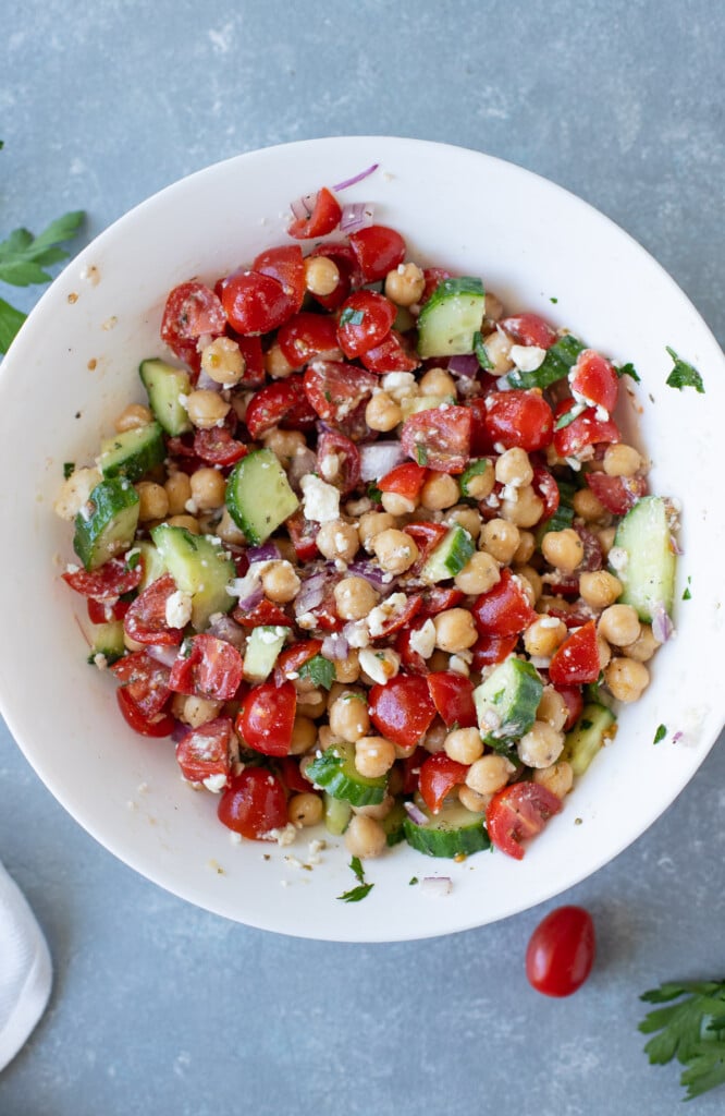 A greek chickpea salad in a large white bowl on a grey background