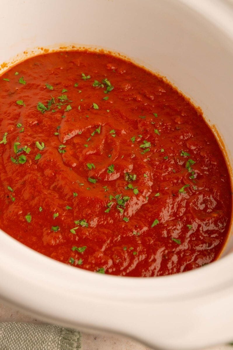 Healthy Crockpot Tomato Sauce in a white crockpot base garnished with chopped fresh herbs.