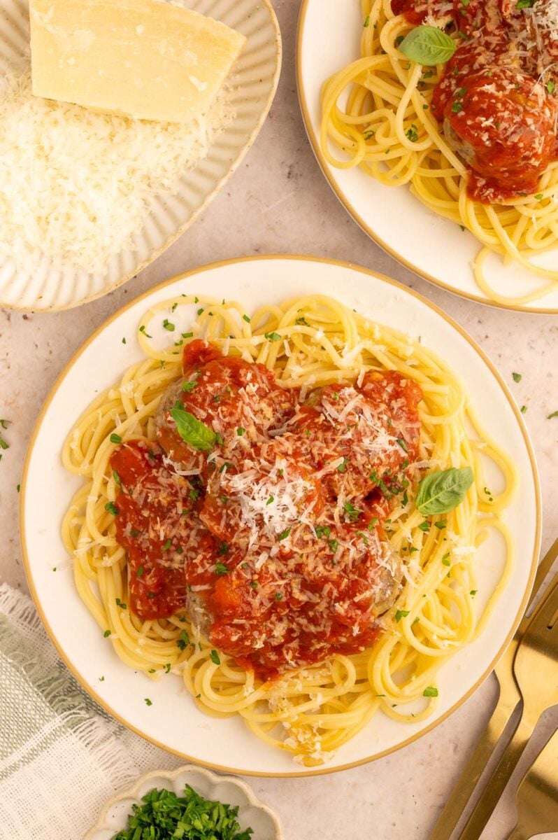 Healthy slow cooker tomato sauce over meatballs and spaghetti on a white plate with grated parmesan cheese on the side. 