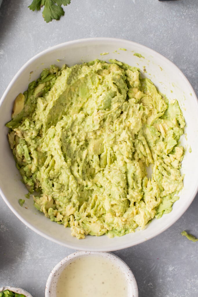 An overhead shot of a white bowl with mashed avocado in it