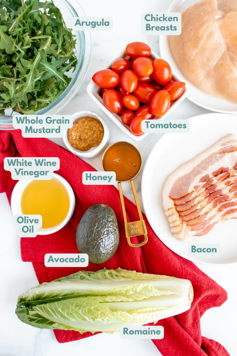 Ingredients for Honey Mustard Chicken Salad in white bowls: chicken breasts, bacon, romaine lettuce, arugula, cherry tomatoes, avocado, honey, whole grain mustard, white wine vinegar, olive oil, salt, pepper