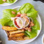 An overhead shot of a lettuce wrap burger on a white plate with fries off to the side