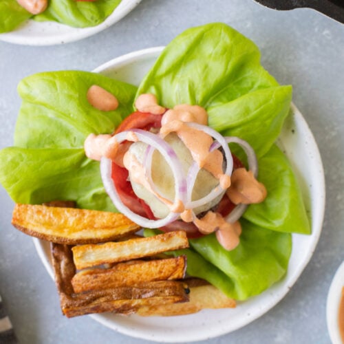 An overhead shot of a lettuce wrap burger on a white plate with fries off to the side