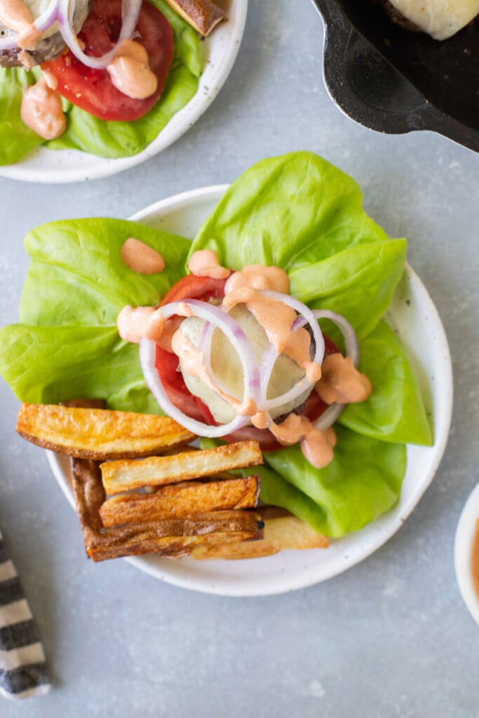 An overhead shot of a lettuce wrap burger on a white plate with fries off to the side