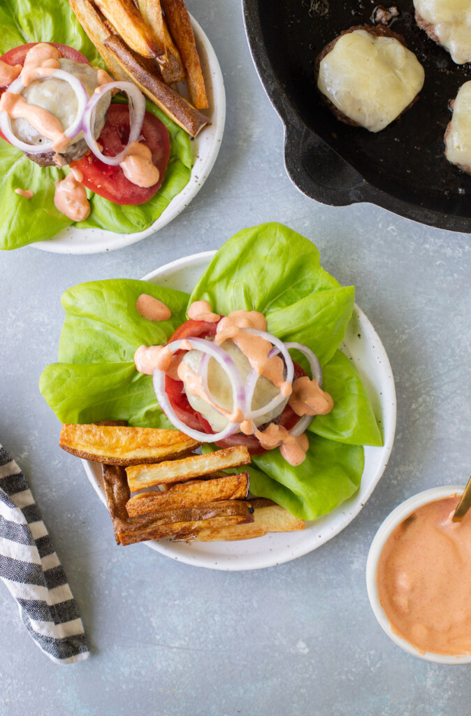 Lettuce Wrap Burgers on a grey background with cooked burgers and sauce on the side.