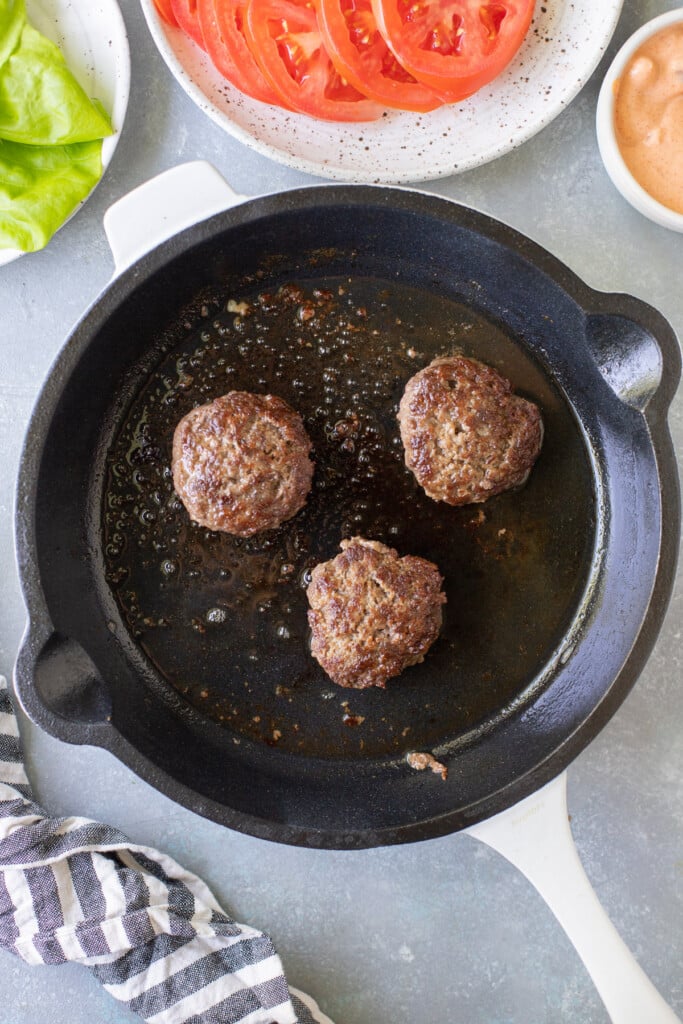 lettuce wrap burgers being seared in a white cast iron pan
