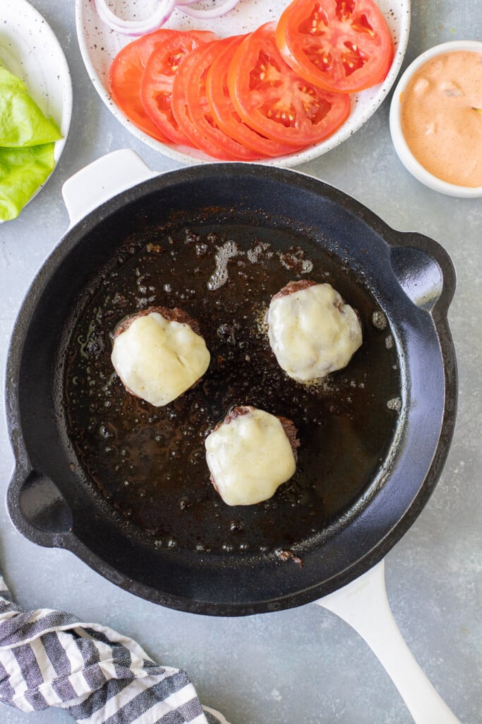 cheese being added to lettuce wrap burgers in a white cast iron pan
