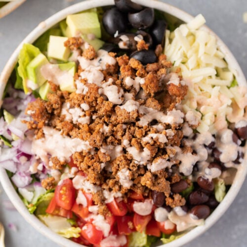 A close up of healthy taco salad in a white bowl topped with a creamy taco dressing