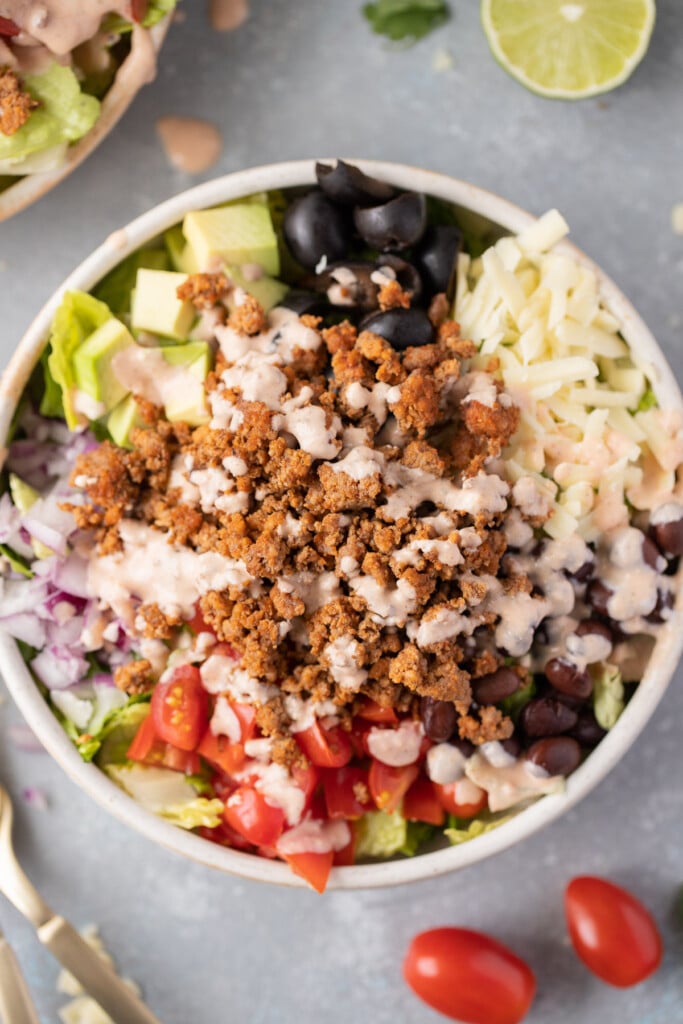 A close up of healthy taco salad in a white bowl topped with a creamy taco dressing