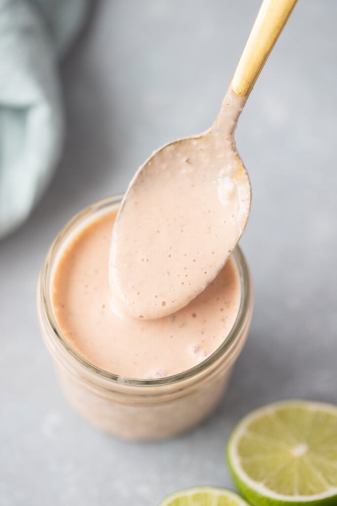 Creamy Taco Dressing in a mason jar with a spoon taking a scoop out with lime slices on the side