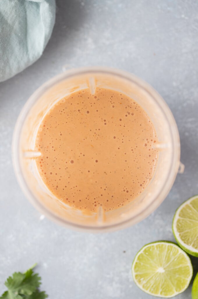 An overhead shot of a creamy salsa dressing in a small blender with sliced limes on the side