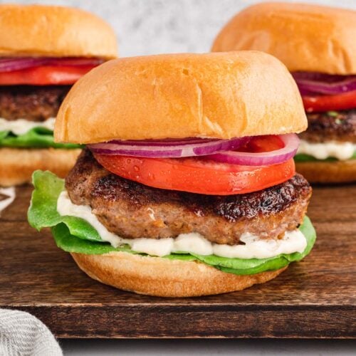 3 Turkey Burgers (burger, bun, tomato, lettuce and mayo) on a wooden cutting board