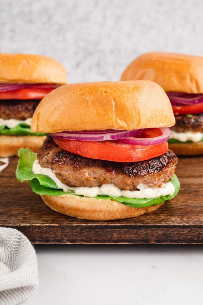 3 Turkey Burgers (burger, bun, tomato, lettuce and mayo) on a wooden cutting board