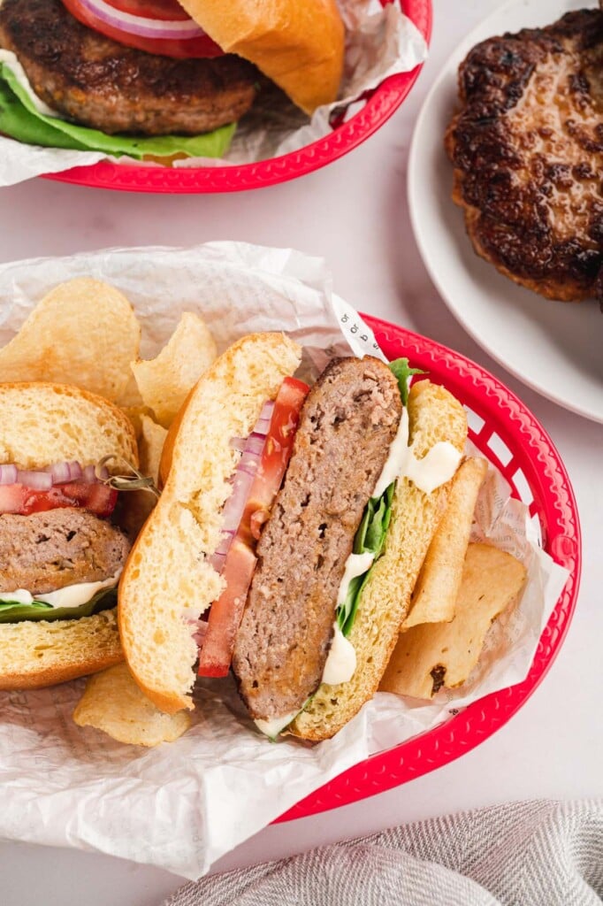 A turkey burger on a bun with tomato, red onion, lettuce and mayo that has been cut in half in a red basket with a paper liner