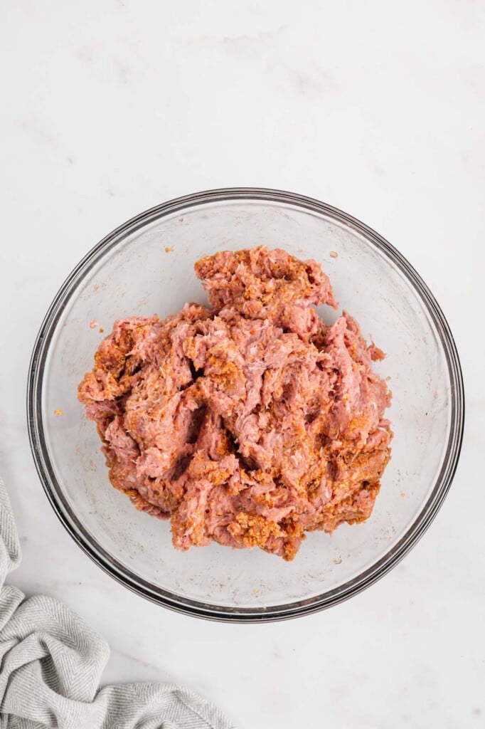 Ingredients for healthy turkey burger in a clear bowl on a white background after being mixed together