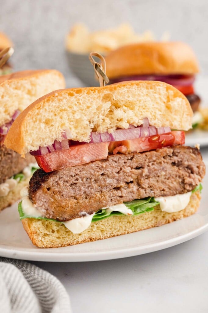A turkey burger on a bun with red onion, tomato, lettuce, and mayo that has been cut in half on a white plate