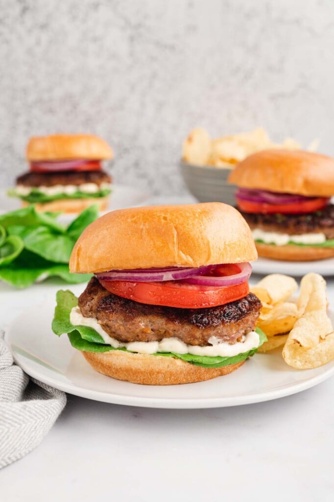 3 Turkey Burgers (burger, bun, tomato, lettuce and mayo) on white plates with chips on the side