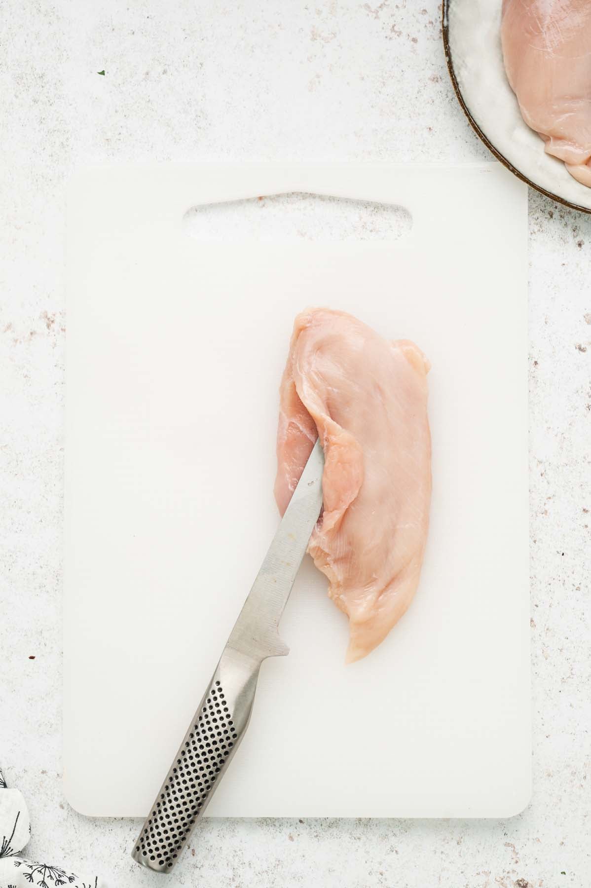 A chicken breast being sliced horizontally to make a pocket for stuffing.