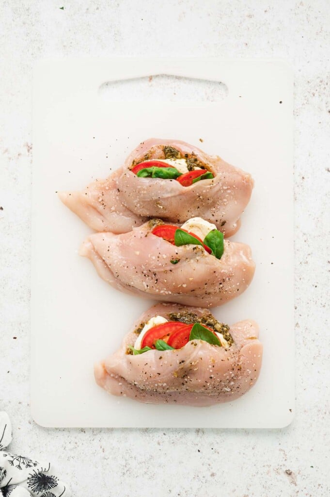 Three raw caprese stuffed chicken breast on a white cutting board