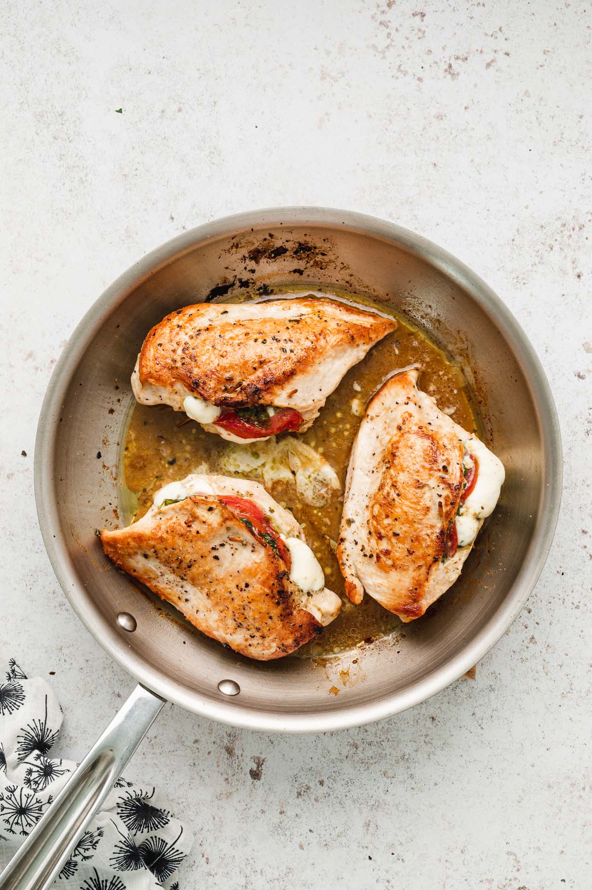 An overhead shot of three seared stuffed chicken breasts in an oven-safe skillet.