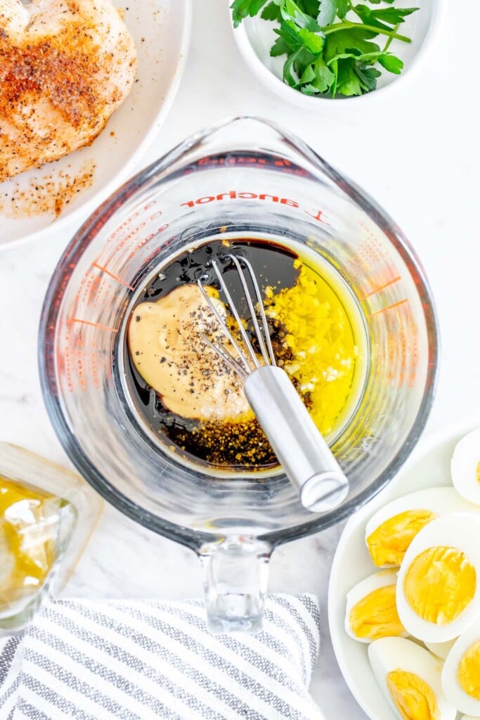 Ingredients for creamy balsamic salad dressing in a clear pyrex measuring cup before being whisked with a whisk sitting in the mixture