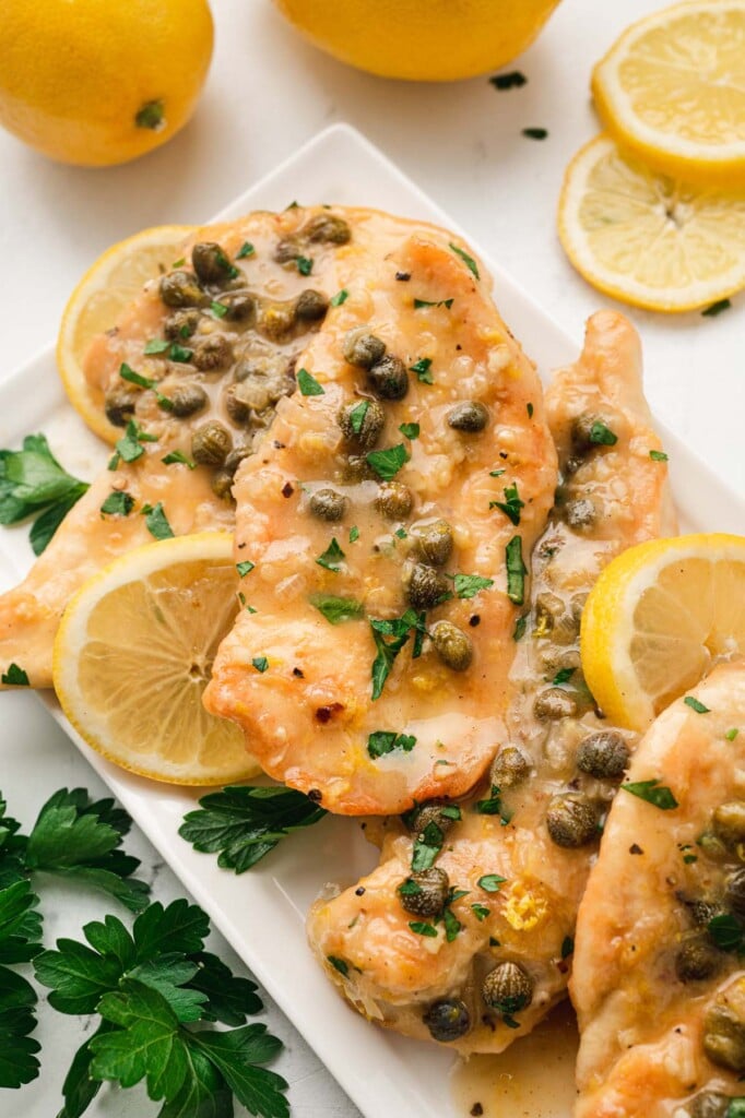 Chicken Piccata on a white platter with lemons in the background