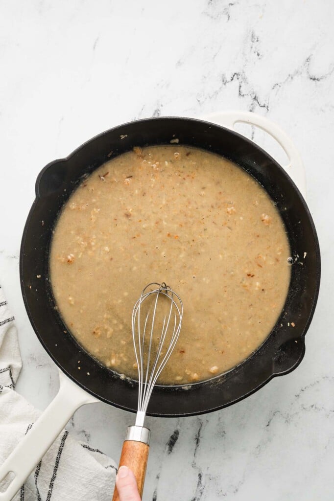 chicken piccata sauce getting whisked in a cast iron pan on a white background