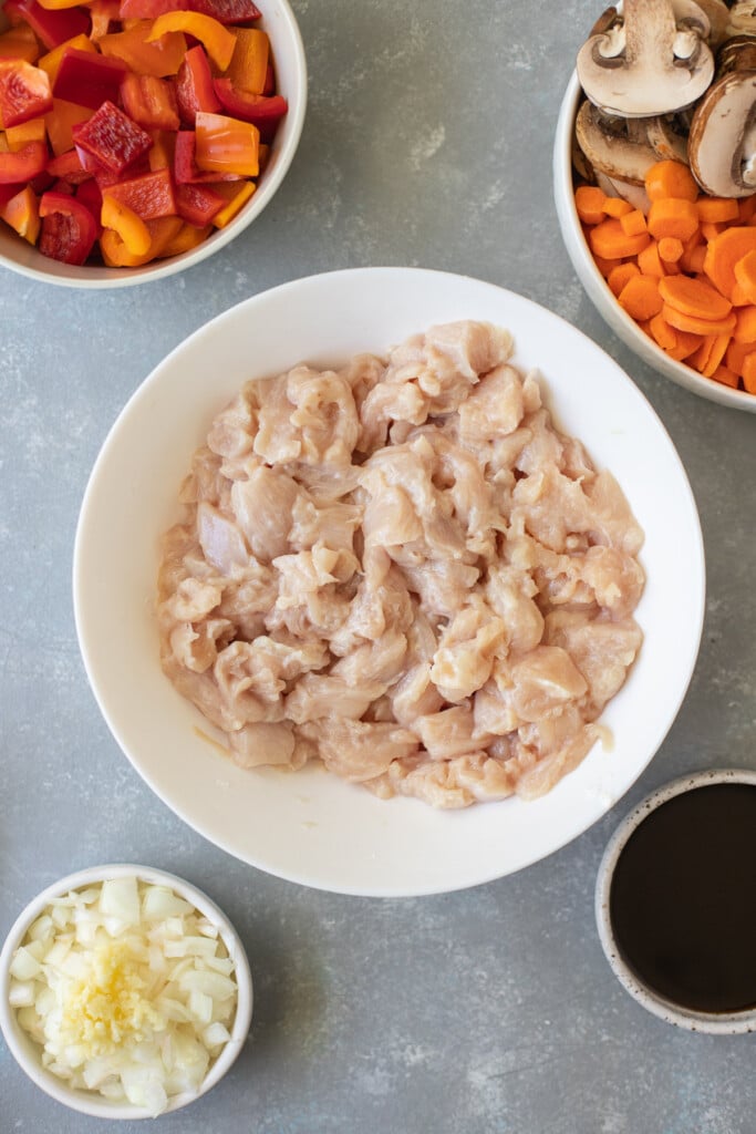 Chicken pieces in a white bowl with stir fry vegetables on the side on a grey background