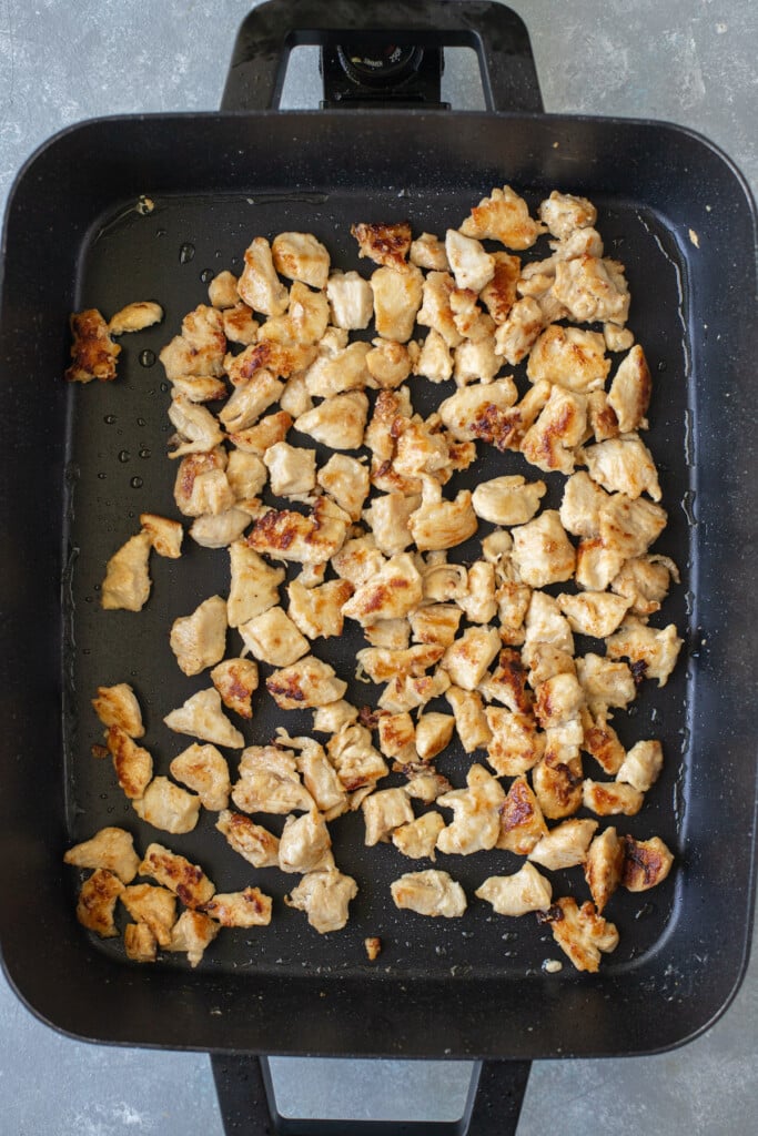 Chicken pieces on a large electric frying pan that have been browned 