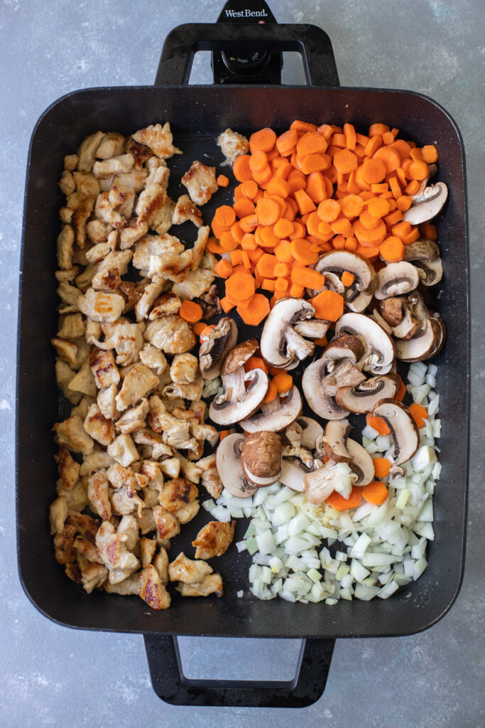 Chicken on half an electric frying pan with carrots, onion, garlic, mushrooms on the other half getting stir fried