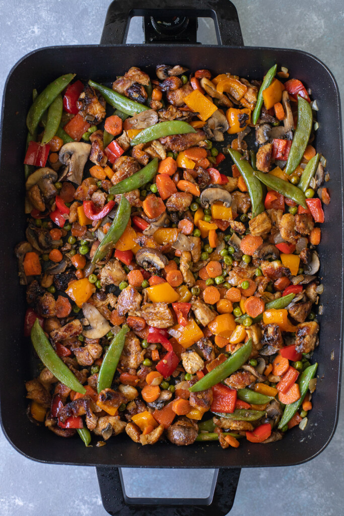 An electric frying pan filled with chicken stir fry on a grey background