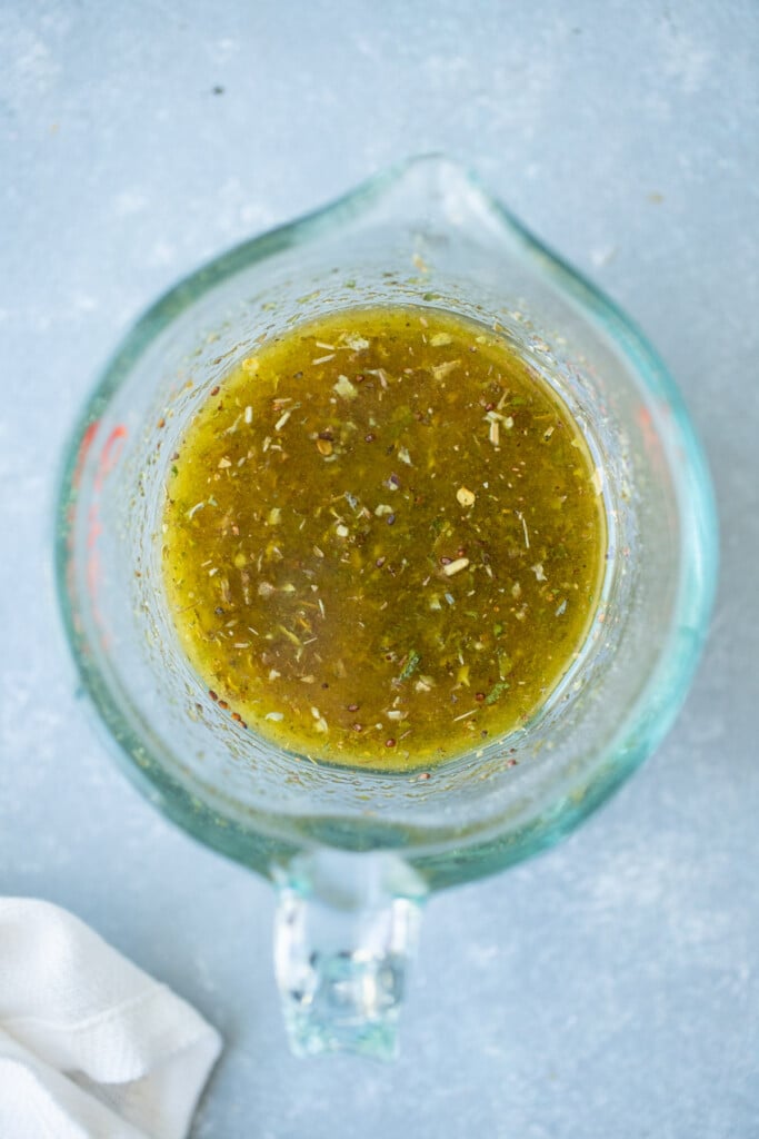 Marinade for grilled chicken thighs in a clear measuring cup on a grey background