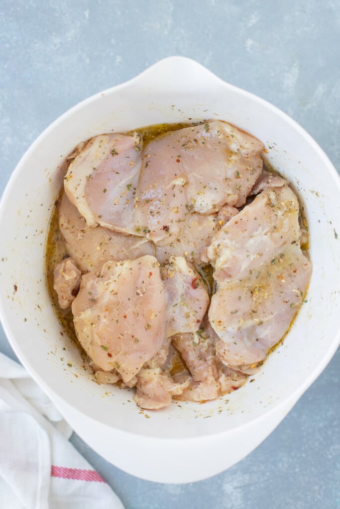 Boneless chicken thighs marinating in a large white bowl on a grey background