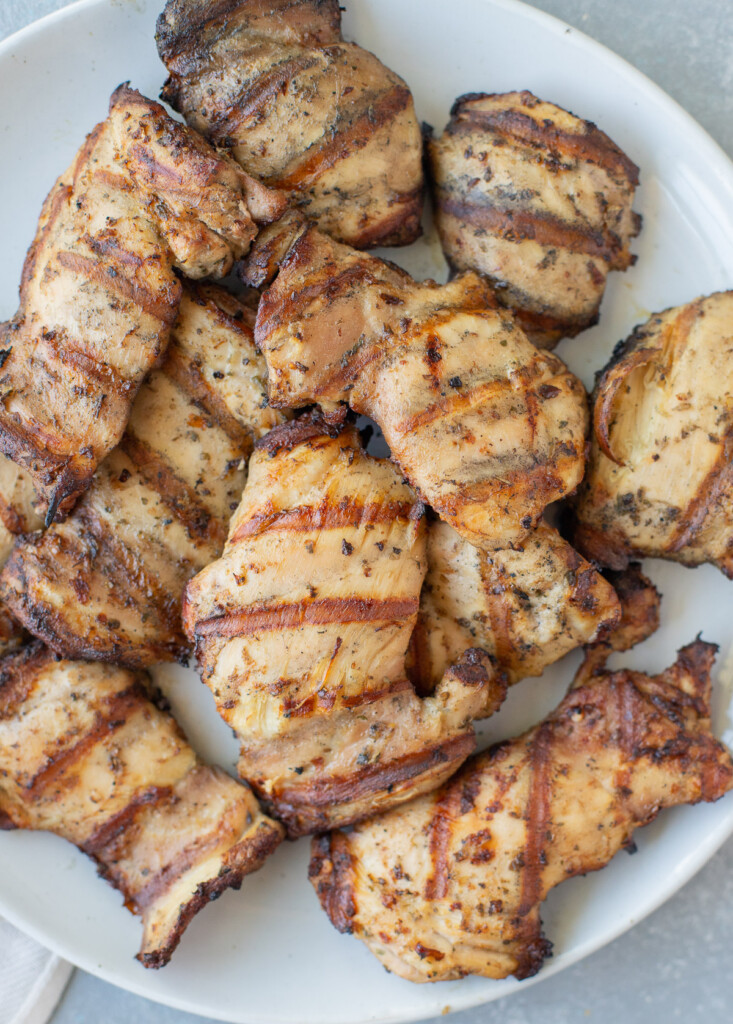 A close up of grilled boneless chicken thighs on a white plate