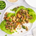 Two Ground Beef Lettuce Wraps on a white plate with bowls of green onions and dipping sauce on the side