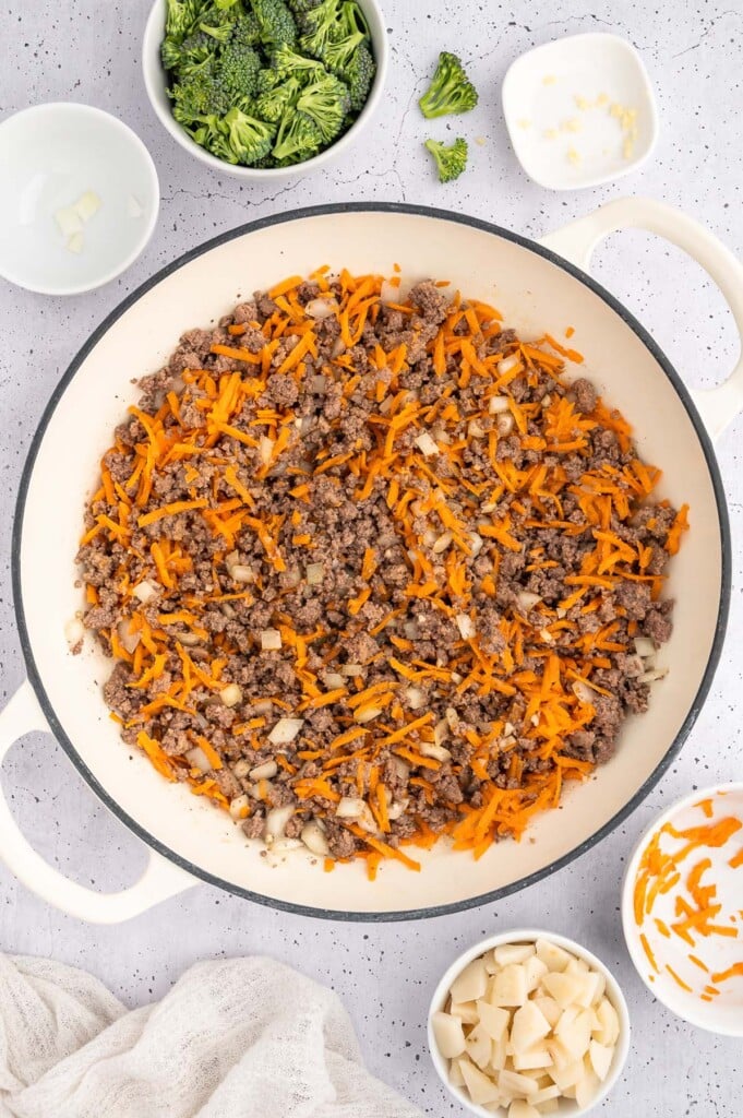Ground beef, onion, garlic, and carrots in a dutch oven after cooking with more ingredients for ground beef lettuce wraps on the side