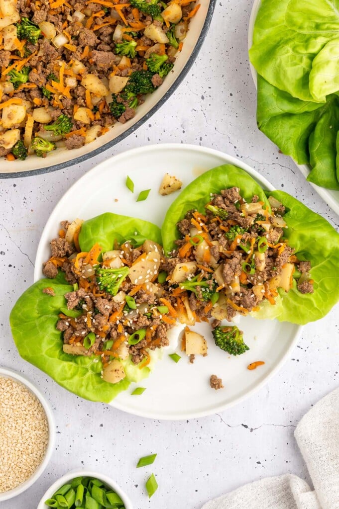 Two Ground Beef Lettuce Wraps on a white plate with the pan of wrap filling on the side