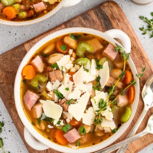 A white bowl of ham white bean soup on a wooden cutting board with another bowl on the side
