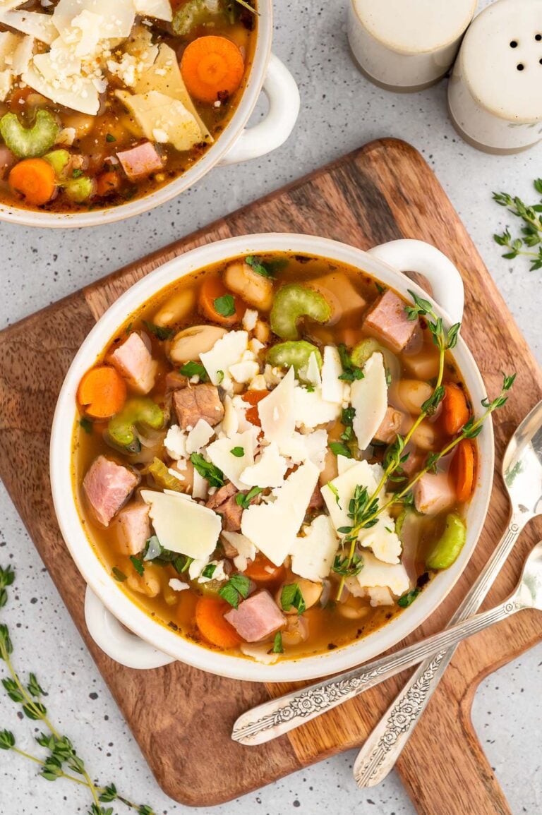 A white bowl of ham white bean soup on a wooden cutting board with another bowl on the side