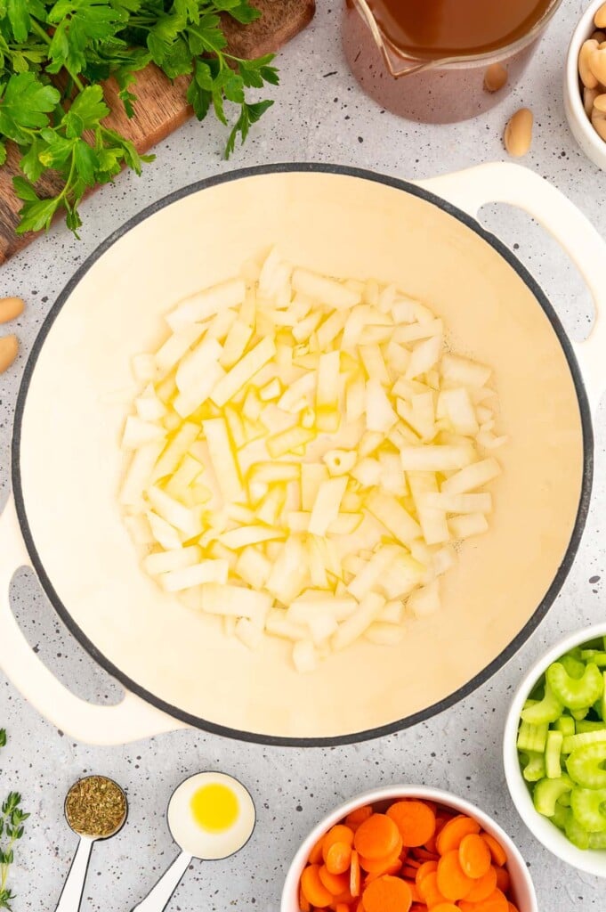 Diced onions in olive oil in a dutch oven with more ingredients for ham white bean soup