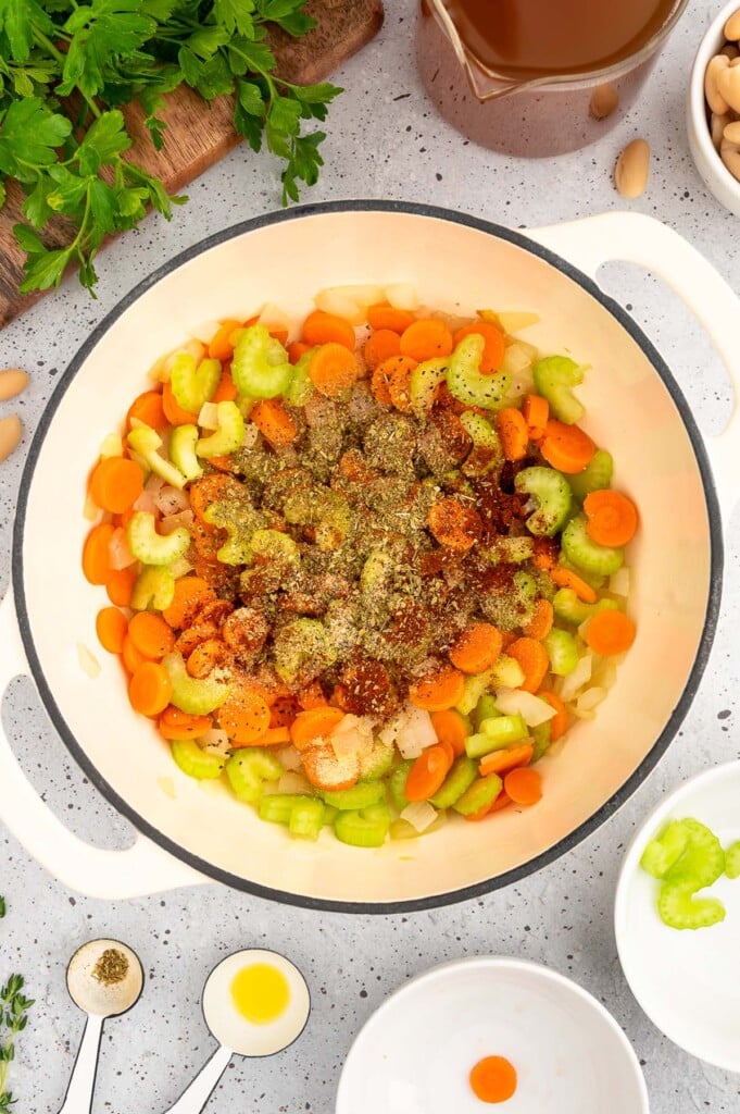 Sliced carrots, celery, and spices added to sauteed onions in a dutch oven to make ham bean soup