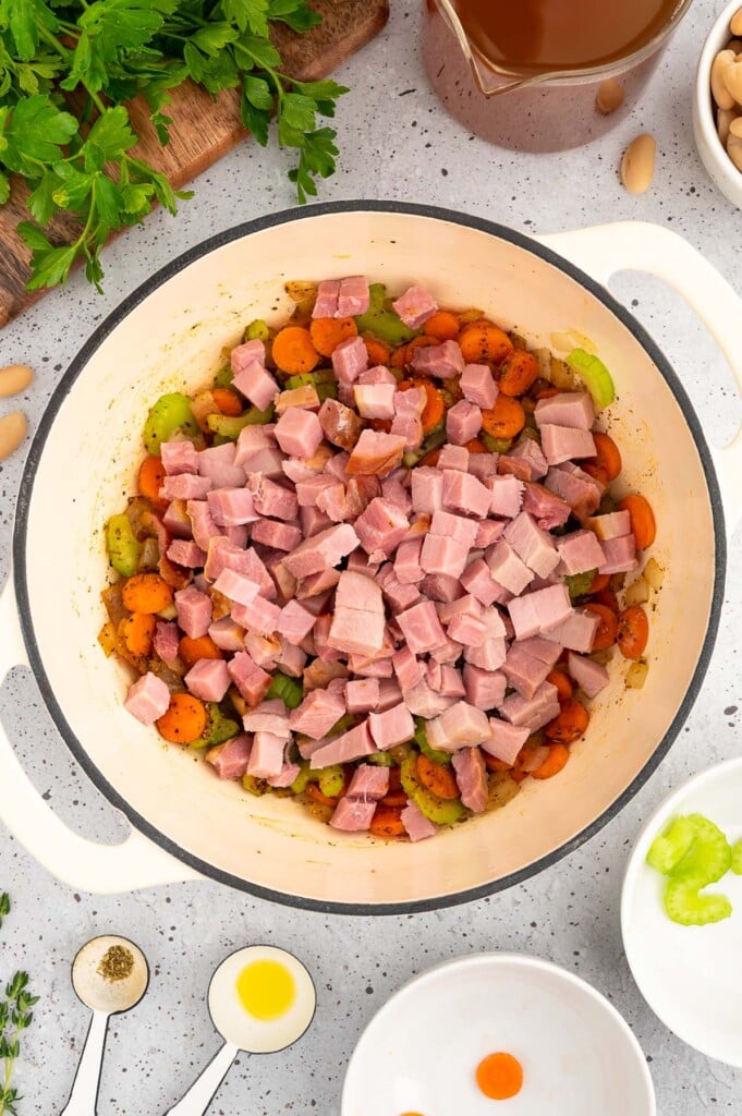 Diced ham added on top of sauteed veggies in a dutch oven to make ham and white bean soup
