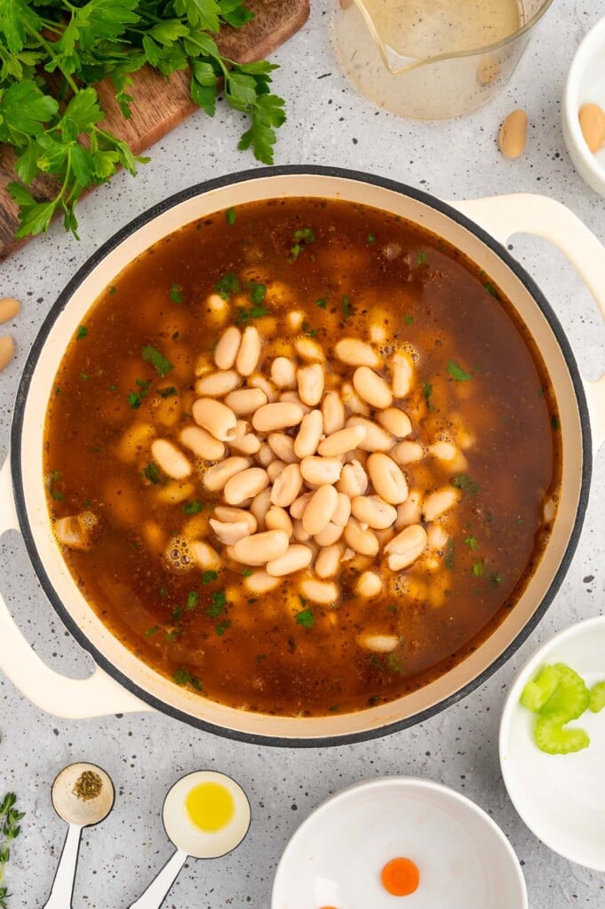 Broth and cannellini beans added to a dutch oven with other ingredients for ham white bean soup