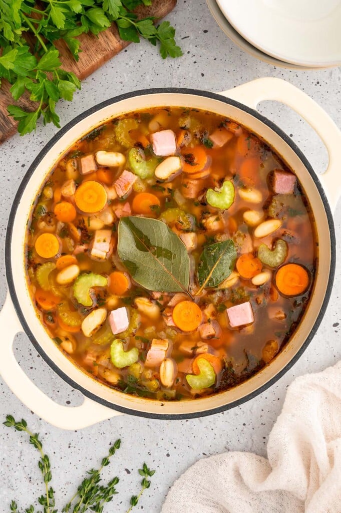 Ham white bean soup in a dutch oven with bay leaves on top on a white counter