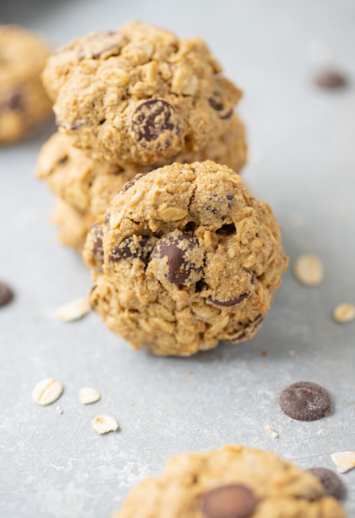 An oatmeal chocolate chip cookie leaning against a stack of cookies on a grey counter
